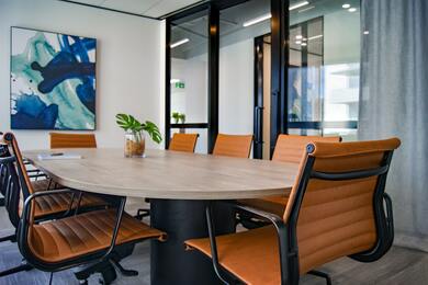 salle de réunion d'une entreprise avec une grande table entourée de chaises roulantes, peinture abstraite dans les tons bleus au mur, et baie vitrée avec porte d'entrée sur le mur gauche